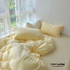 an unmade bed with yellow pillows in front of a window