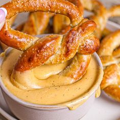 pretzels being dipped with mustard in a bowl on a plate next to other pretzels