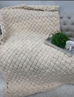 a blanket and cup on a couch with a plant in the corner next to it