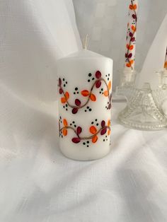 two white candles with orange and black designs on them sitting next to a glass candle holder