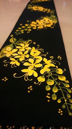 a black table runner with yellow flowers painted on the side and green leaves in the middle