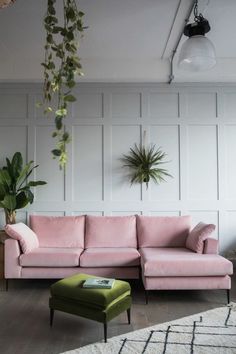 a living room with pink couches and plants hanging from the ceiling, along with a green footstool