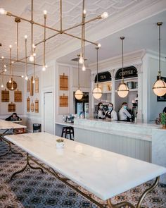 the interior of a coffee shop with white tables and gold chandeliers hanging from the ceiling