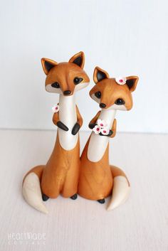 two little foxes sitting next to each other on top of a white table with pink flowers