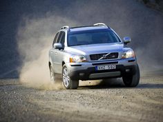 a silver suv driving down a dirt road with dust coming from the front tire and hood