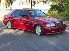 a red car is parked on the side of the road near some trees and water