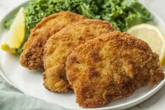 two fried chicken patties on a plate with broccoli and lemon wedges