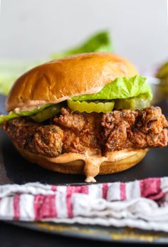 a chicken sandwich with lettuce and pickles on a black plate next to a red and white napkin