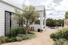 a white house with trees and plants around it's perimeter, next to a gravel path