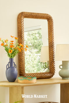 a mirror sitting on top of a wooden table next to a vase filled with flowers