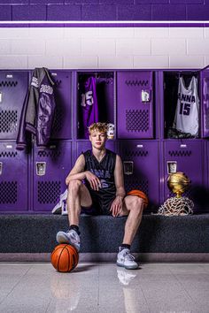 a man sitting on a bench in front of lockers with basketballs and jerseys