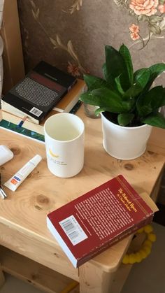 a wooden table topped with books and a cup filled with liquid next to a plant