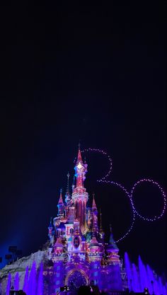 the castle is lit up at night with purple lights