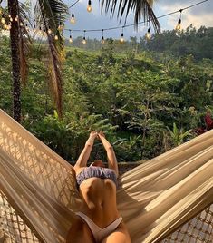 a woman laying in a hammock on top of a lush green forest