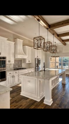 a large kitchen with white cabinets and wood flooring is pictured in this image, there are two chandeliers hanging from the ceiling