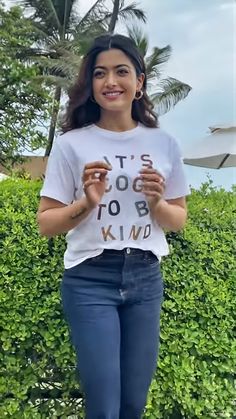 a woman standing in front of some bushes wearing a t - shirt that says it's too to be kind