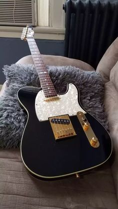 a black guitar sitting on top of a couch next to a pillow and a teddy bear