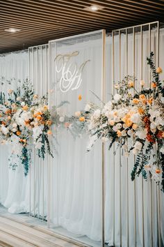 flowers are arranged on the side of a wall with white drapes and gold letters