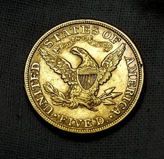 a gold coin with an eagle on the front and bottom, sitting on a black cloth