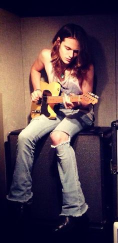 a woman sitting on top of a guitar in front of a wall with guitars behind her