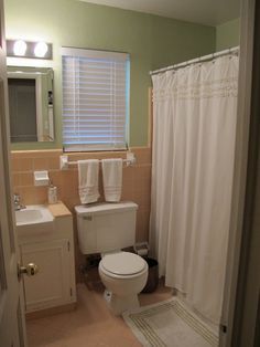 a white toilet sitting in a bathroom next to a sink and shower curtain with the light on