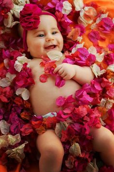 a baby is laying down with flowers all over her body and smiling at the camera