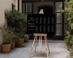 an easel stands in front of a building with potted plants