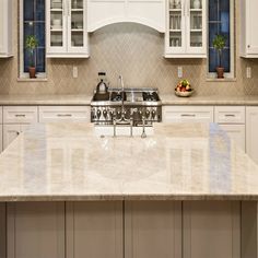 a kitchen with white cabinets and marble counter tops