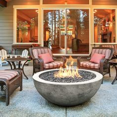 an outdoor fire pit sitting on top of a patio next to chairs and tables with cushions