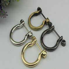 three pairs of gold, silver and black metal hoop earrings on a white surface with flowers in the background