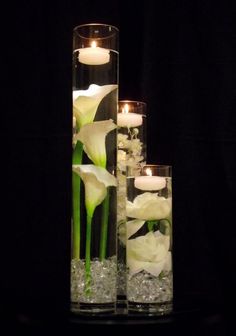 three tall glass vases with flowers and candles in them on a black tablecloth