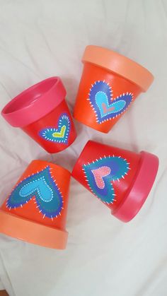 four plastic cups with designs on them sitting on a white bed sheet, one has an orange cup and the other is pink