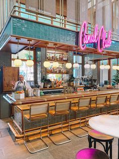 a man standing in front of a bar with neon signs on the wall and chairs around it