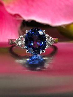 a blue and white diamond ring sitting on top of a pink plate next to a flower