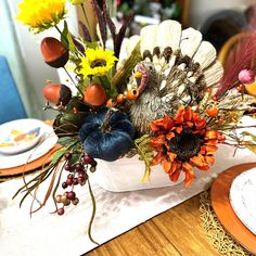 an arrangement of flowers and feathers in a basket on a dining room table with place settings