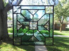 a stained glass window hanging from the side of a tree in front of a house