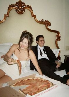 a man and woman sitting on a bed with pizza