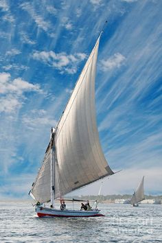 two sailboats sailing in the ocean under a blue sky with wispy clouds