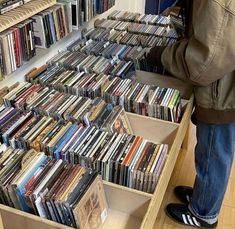 a person standing in front of a large amount of cds on a wooden shelf next to a bookcase