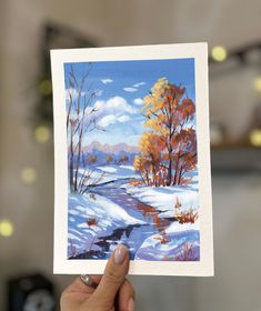 a person holding up a card with a painting of a snowy landscape and trees in the background