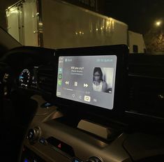 the dashboard of a car with an electronic device on it's display screen, in front of a truck at night