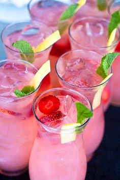 several glasses filled with different types of drinks and garnished with mint leaves, lemon wedges and strawberries