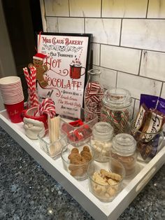 a tray filled with candy and cookies on top of a counter next to a sign that says hot chocolate