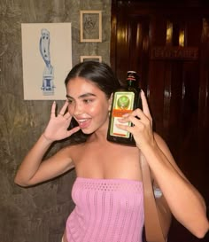 a woman in a pink top holding up a bottle of beer with her right hand