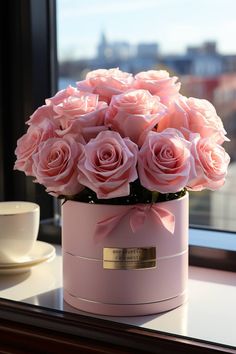 pink roses in a pink vase on a window sill near a cup and saucer