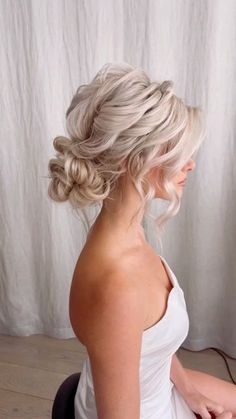 a woman with blonde hair wearing a wedding dress and braid in her hair, looking out the window