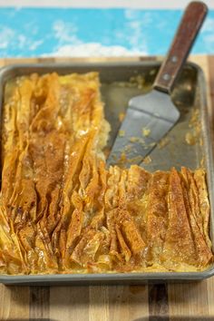 a pan filled with food sitting on top of a wooden table next to a spatula