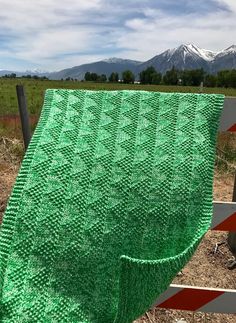 a green blanket sitting on top of a wooden fence next to a field with mountains in the background