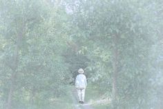 a person walking down a dirt road in the middle of some trees and bushes,