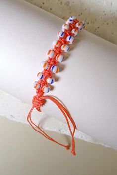 an orange and white beaded bracelet on a woman's arm with red string